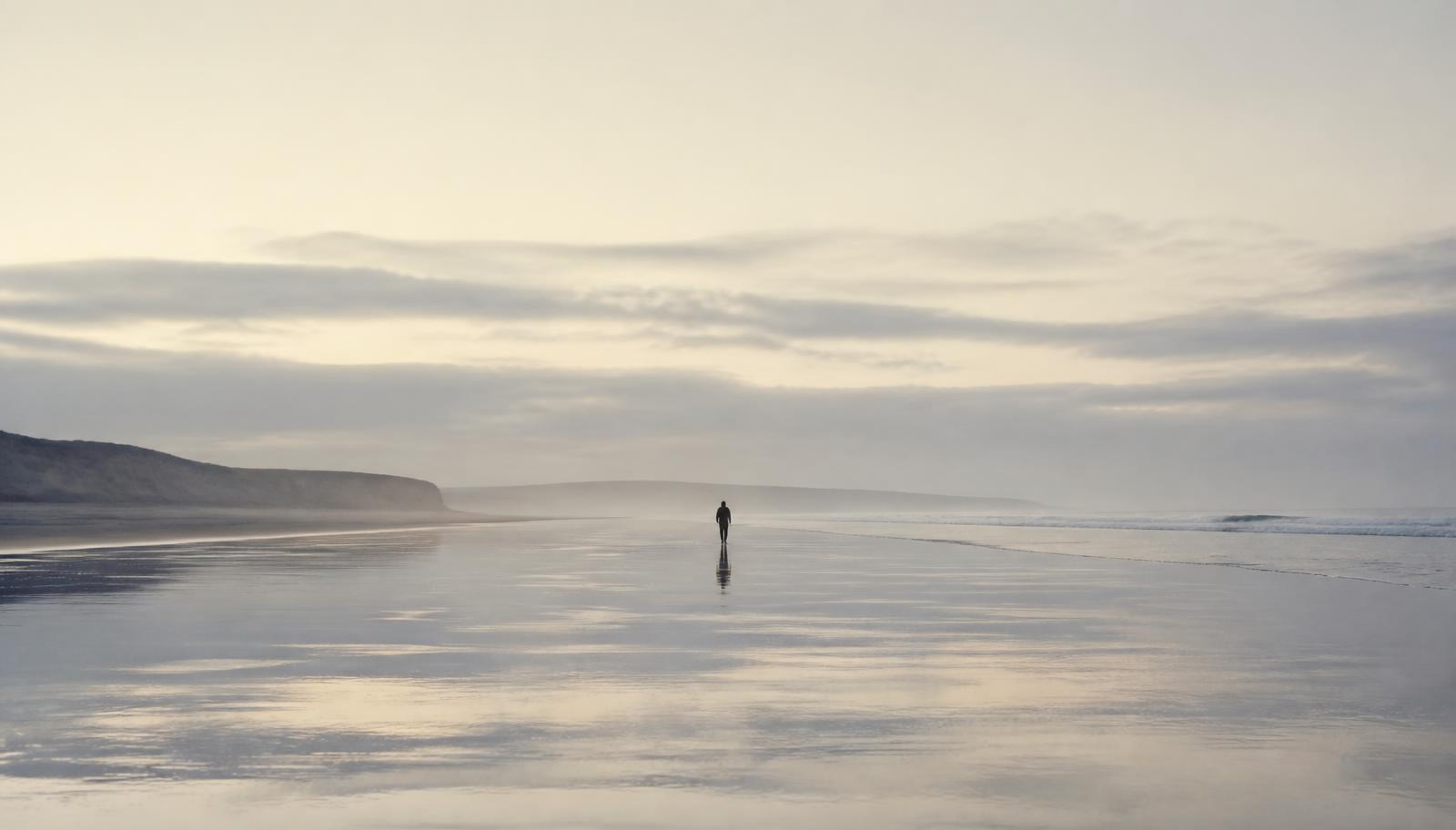 Een eenzame persoon wandelend over een breed, leeg strand bij eb