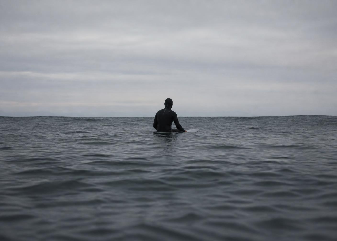 Een eenzame surfer zittend op een plank ver op zee onder een grijze lucht